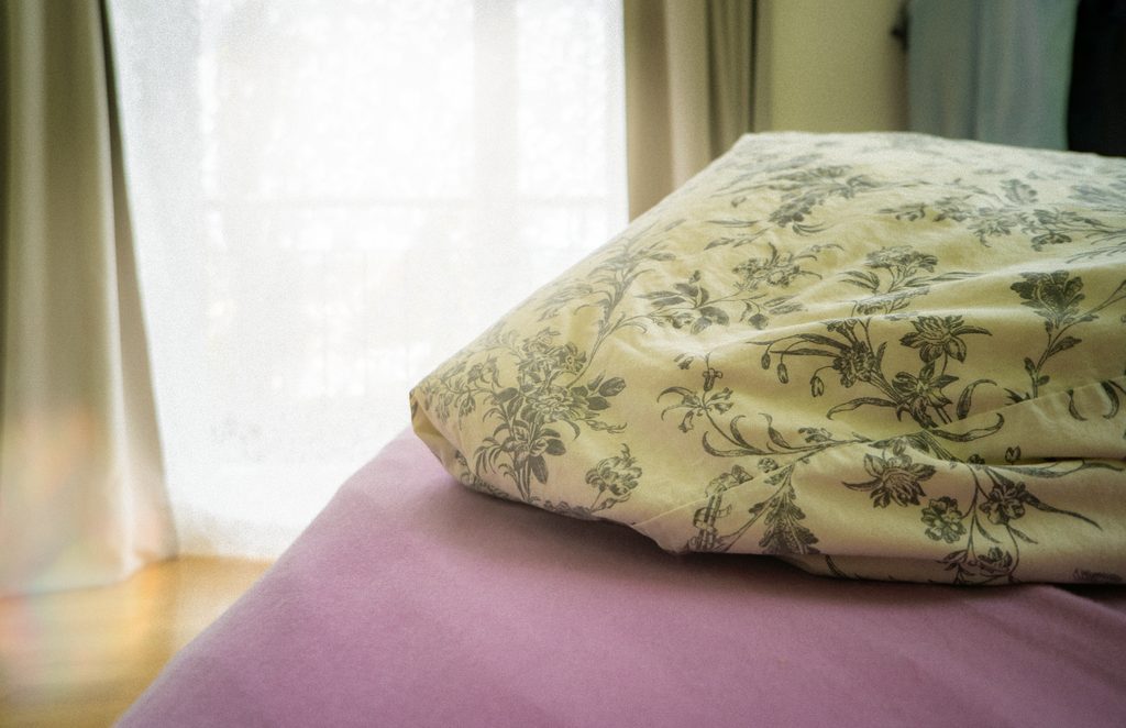 Ungemachtes Bett mit floralem Kissen am Morgenfenster – ruhiger Tagesanfang